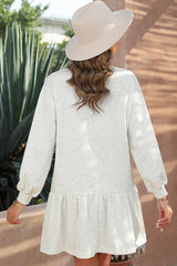 Back view of a woman wearing a light grey long-sleeved drop-waist dress with a ruffled hem and a cream fedora hat.