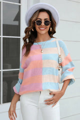 Woman wearing a pastel striped color-block knit sweater, white pants, sunglasses, and a hat