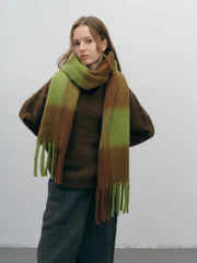 Woman wearing a brown sweater and a green and brown plaid scarf with fringe.