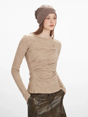 Close-up of a woman wearing a beige long-sleeve knit top with ruched detailing and a beige beanie adorned with studs.