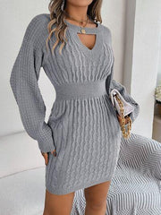 Woman wearing a grey cable knit sweater dress with a keyhole neckline and holding a white clutch.