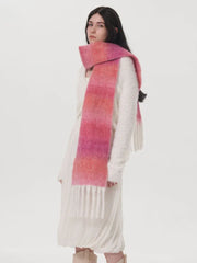 Woman wearing a white sweater and a long pink and orange gradient scarf with fringe.