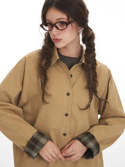 Close-up of a model's face and upper body, showcasing the tan button-down shirt with plaid cuffs and embroidered detail.