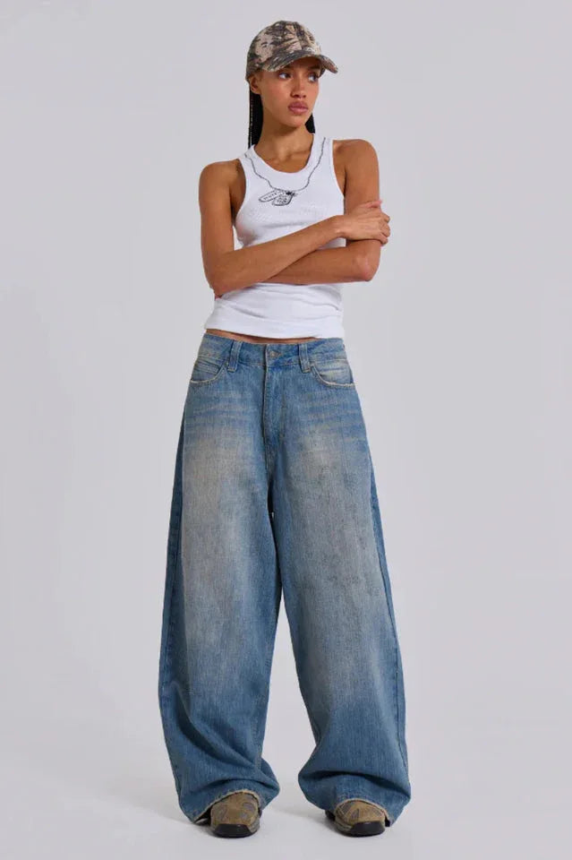 Model wearing loose-fitting light wash denim jeans and a white tank top with a cap.