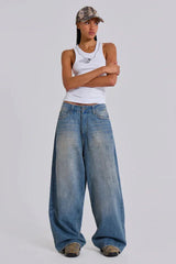 Model wearing loose-fitting light wash denim jeans and a white tank top with a cap.