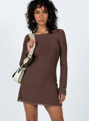 Woman wearing a long sleeve brown mini dress with a boat neckline and a white crossbody bag, front view.