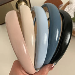 A hand holding five padded headbands in various colors: pink, cream, light blue, dark blue, and black