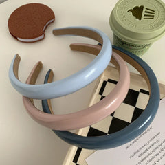 A stack of three padded headbands in pink, light blue, and dark blue on a white surface with decorative items