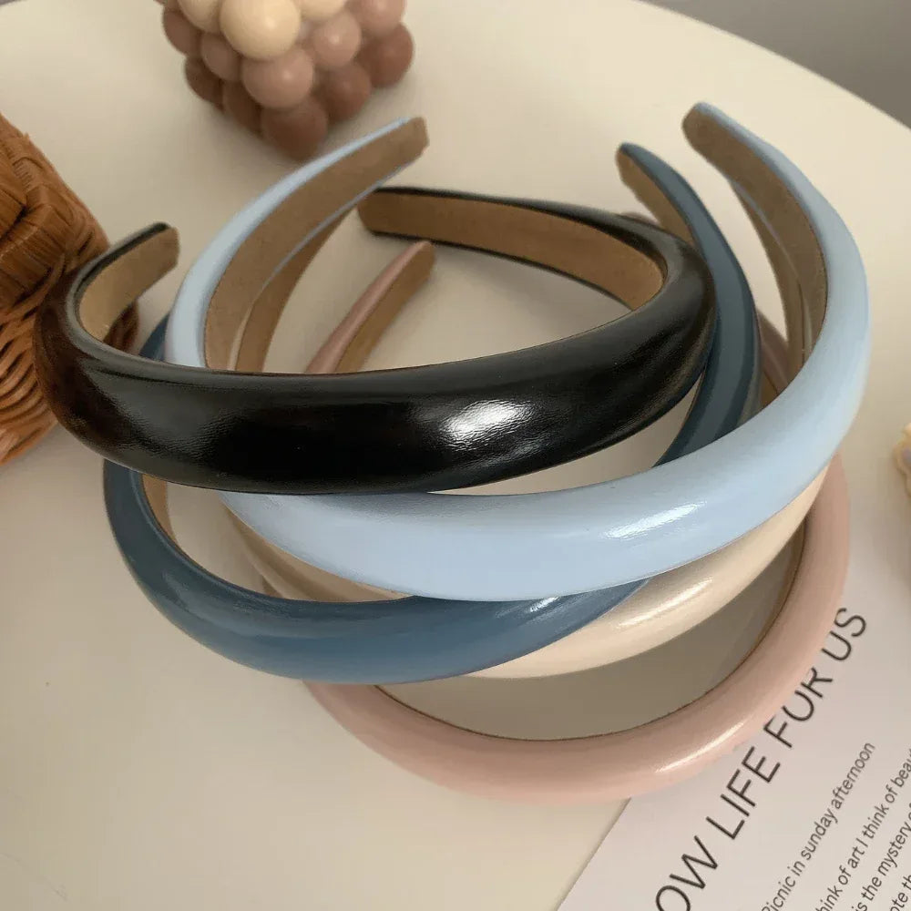 A stack of five padded headbands in pink, cream, light blue, dark blue, and black on a white surface with decorative items
