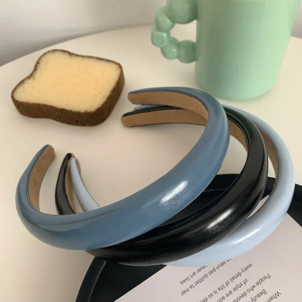 A stack of three padded headbands in black, dark blue, and light blue on a white surface