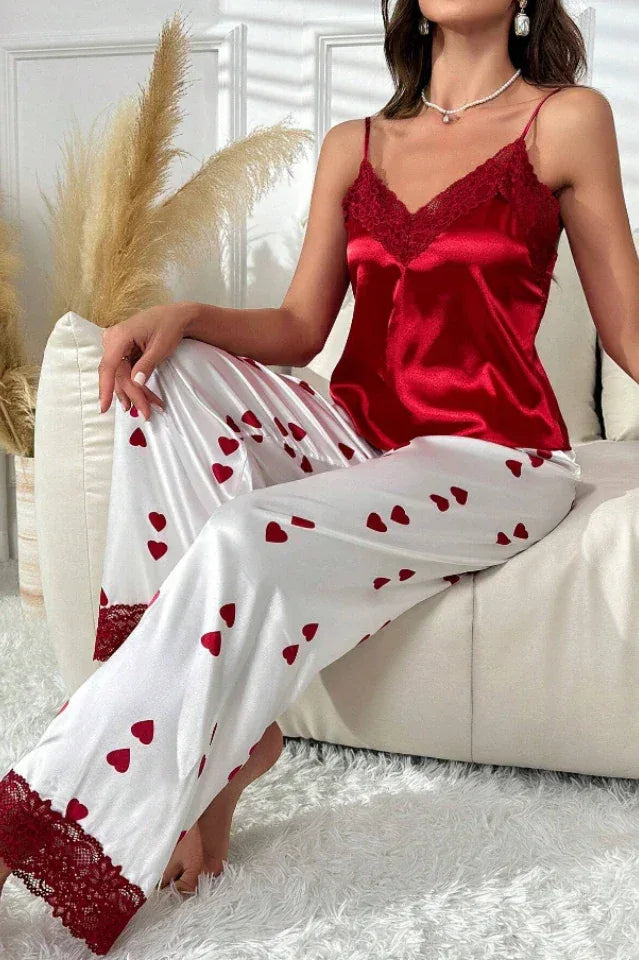 Close-up of a woman wearing red satin camisole and white satin pants with red heart print and lace trim sitting on a couch.