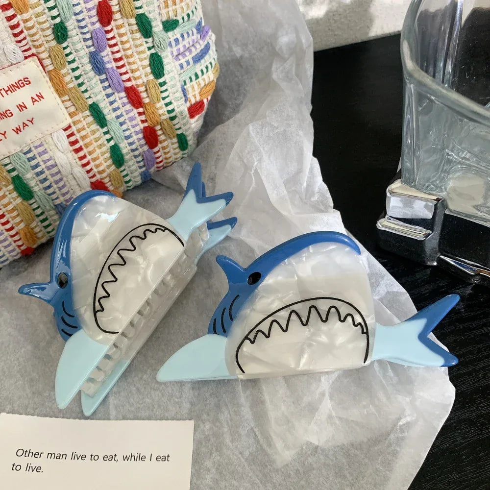 Two blue and white shark hair clips next to a woven bag
