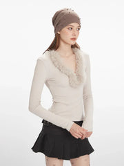 Side view of a woman wearing a cream long-sleeve top with fur trim, a black pleated mini skirt, decorative tights, and black boots, holding a white bucket bag.