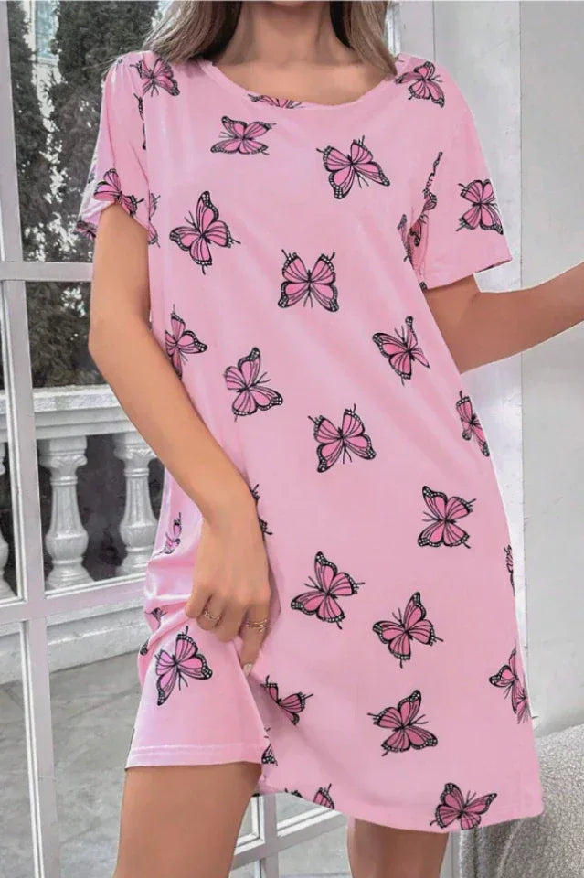 Woman wearing a pink short-sleeve nightgown with a butterfly print, standing indoors.