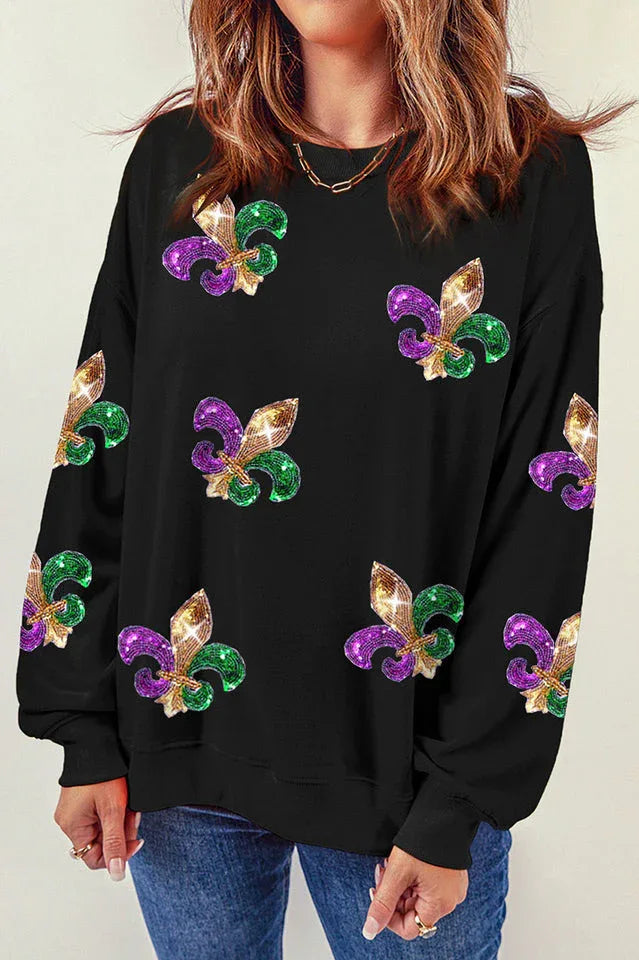 Front view of a woman wearing a black long-sleeved sweatshirt featuring a dense pattern of colorful sequin fleur-de-lis embellishments.