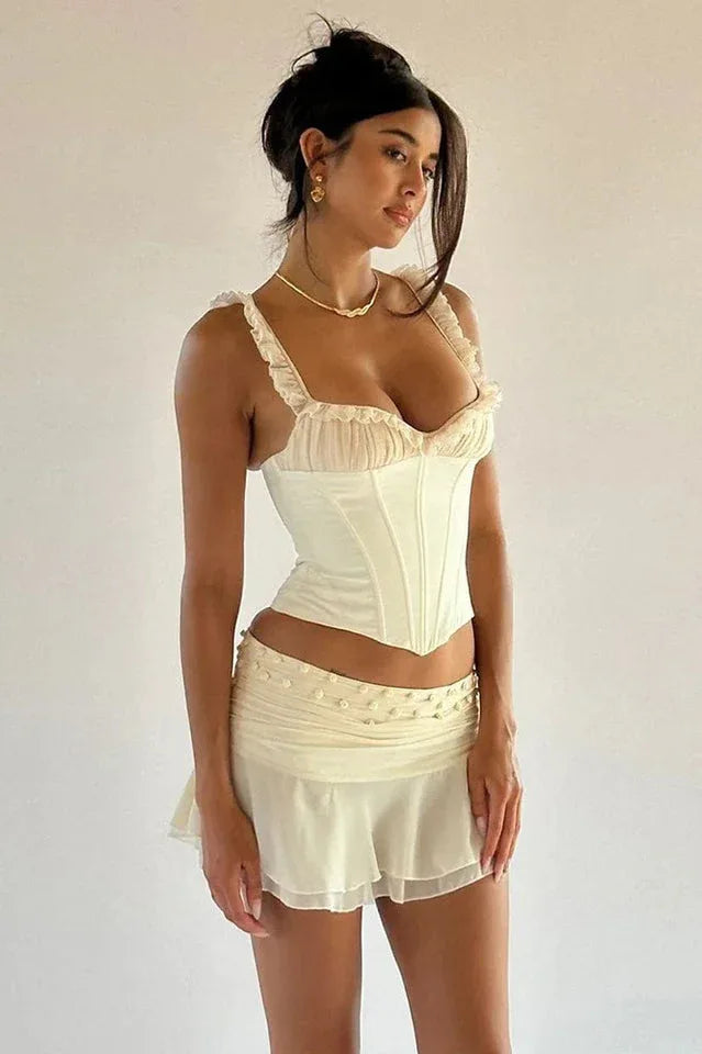 Full body shot of a woman in a white corset top and mini skirt against a plain background.