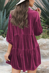 Back view of a woman wearing a magenta velvet babydoll dress, showcasing the tiered skirt and puff sleeves.