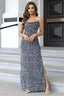 Woman wearing a floor-length, spaghetti strap, sequined gray dress with a high slit, standing on stairs.