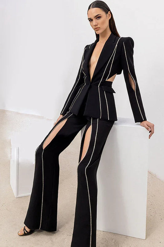 Woman wearing a black suit with cut-out details and decorative trim, posing on a white cube.
