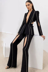 Woman wearing a black suit with cut-out details and decorative trim, posing on a white cube.