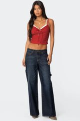 Full body front view of a woman wearing a red cropped tank top with lace trim and dark wash wide-leg jeans.
