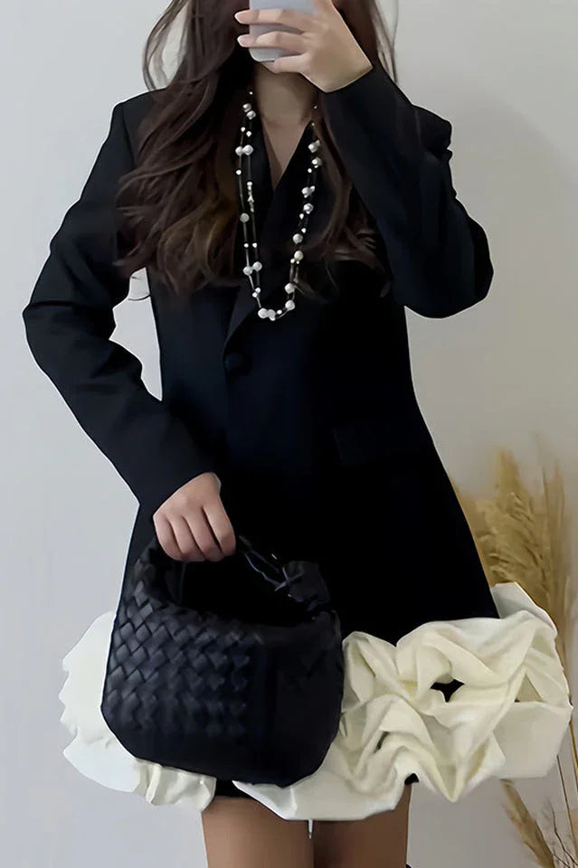 Woman holding a black woven handbag while wearing a black double-breasted blazer dress with a white ruffled hem