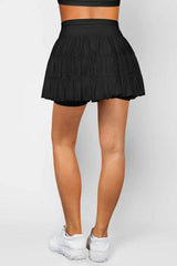 Back view of a woman wearing a black tiered ruffle skirt with built-in shorts.