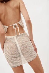 Back view of a woman wearing a cream crocheted halter top with tie closure and a matching mini skirt.
