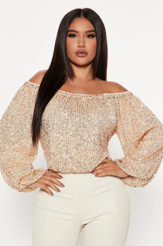 Woman wearing a champagne sequined off-the-shoulder top with balloon sleeves and white pants, front view