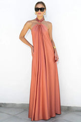 Woman in a coral satin halter maxi dress standing against a white wall.