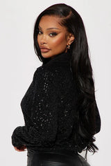 Woman wearing a black sequined cropped shirt and black faux leather pants, close-up back view.
