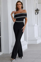 Woman in a black off-the-shoulder jumpsuit with geometric trim posing outdoors.