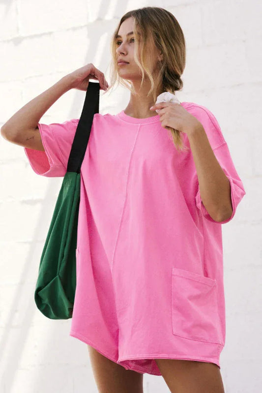 Woman wearing a bright pink oversized tunic with short sleeves and pockets, carrying a green tote bag.