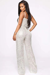 Back view of a woman wearing a silver sequined sleeveless wrap jumpsuit with a self-tie waist belt and wide legs.