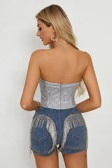 Back view of a woman in a silver sequined corset top and denim shorts with fringe detail