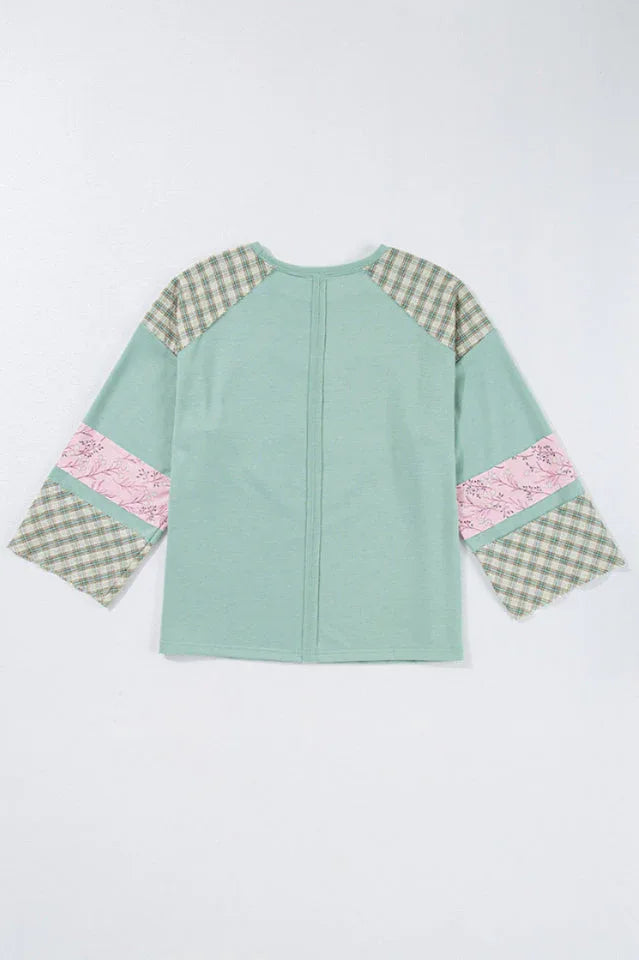 Flat lay of the back of a mint green long-sleeved top with a heart applique and plaid patchwork sleeves.