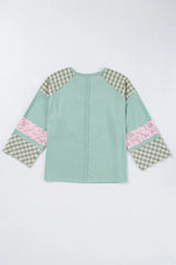 Flat lay of the back of a mint green long-sleeved top with a heart applique and plaid patchwork sleeves.