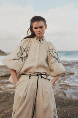 Model posing in a linen co-ord set with embroidered flowers by the ocean