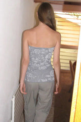 Rear view of a woman walking away from the camera, wearing a light gray strapless top with a white floral pattern and vertical ribbing, paired with gray cargo pants.