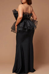 Rear view of a plus-size woman wearing a black strapless formal gown with a ruffled peplum bodice and mermaid skirt.