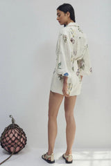 Woman wearing a white floral print button-down shirt with puffed sleeves and matching high-waisted shorts, back view