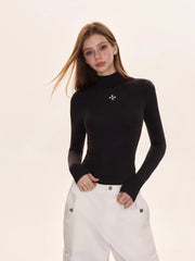 Woman wearing a black turtleneck top with a white embroidered cross, paired with white cargo pants.