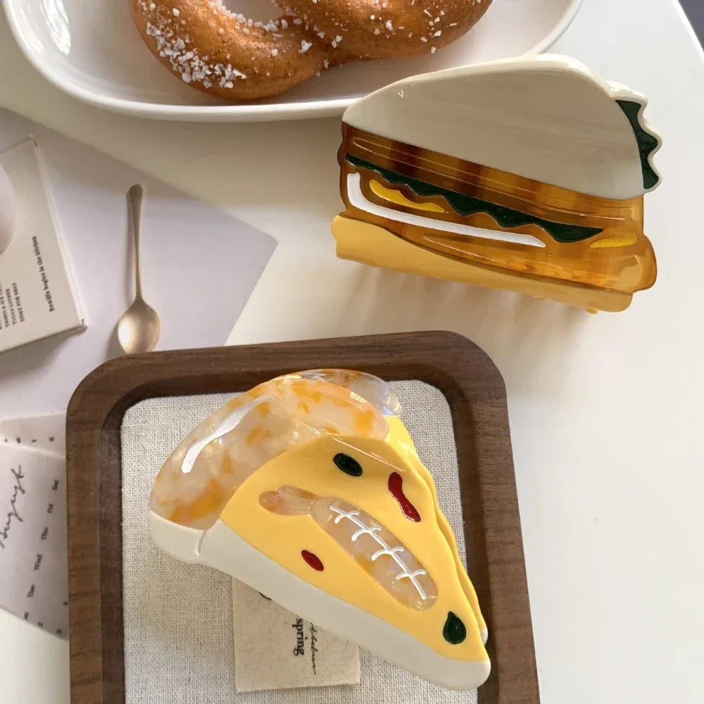 acrylic slice of pizza hair clip and a sandwich hair clip arranged on a white plate with pretzels in the background