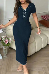 Woman wearing a navy blue ribbed knit midi dress with white contrast trim and a lace-up V-neck, standing in a living room.