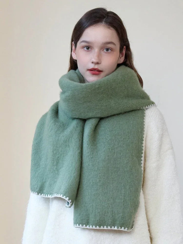Woman wearing an oversized green scarf with a white fringed edge and a cream-colored sweater, looking forward.