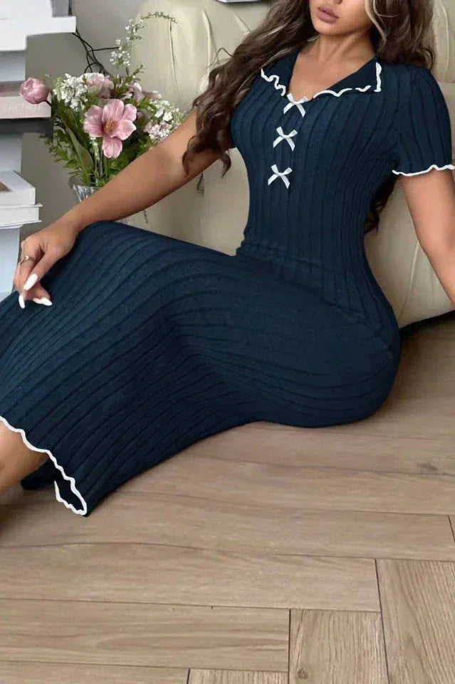 Woman sitting on a sofa wearing a navy blue ribbed knit midi dress with white contrast trim and a lace-up V-neck.