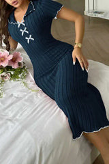 Woman lying on a bed wearing a navy blue ribbed knit midi dress with white contrast trim and a lace-up V-neck.