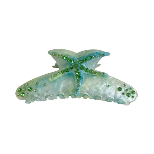 Close-up of a blue and white marbled resin hair claw clip shaped like a starfish, adorned with green rhinestones.