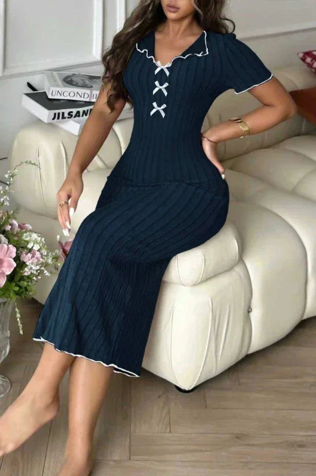 Woman sitting on a sofa wearing a navy blue ribbed knit midi dress with white contrast trim and a lace-up V-neck.