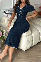 Woman sitting on a sofa wearing a navy blue ribbed knit midi dress with white contrast trim and a lace-up V-neck.